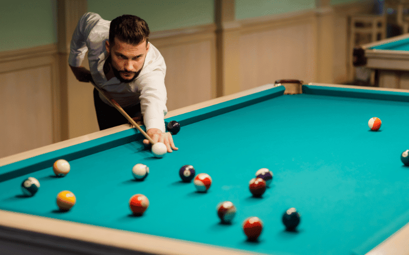 A crowded billiards tournament with intense players and enthusiastic spectators. The room is filled with the sound of balls clinking and the occasional cheer